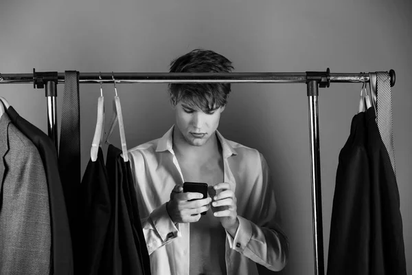 Man with muscular torso at wardrobe hanger with phone — Stock Photo, Image