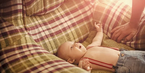 Pojke i jeans med hängslen ligga i fåtölj — Stockfoto