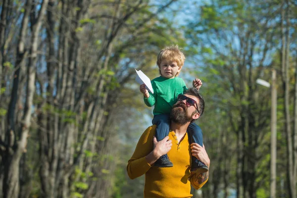 Padre dar hijo a cuestas lanzamiento avión de papel de juguete. Niño pequeño juega con juguete en el parque. Arriba, arriba y lejos — Foto de Stock