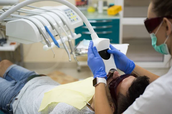 Jeune homme souriant après visite dentiste sur fond flou lumineux. Un bel homme au cabinet de dentistes. Dentiste examinant les dents des patients à la clinique. Comparaison après blanchiment des dents . — Photo