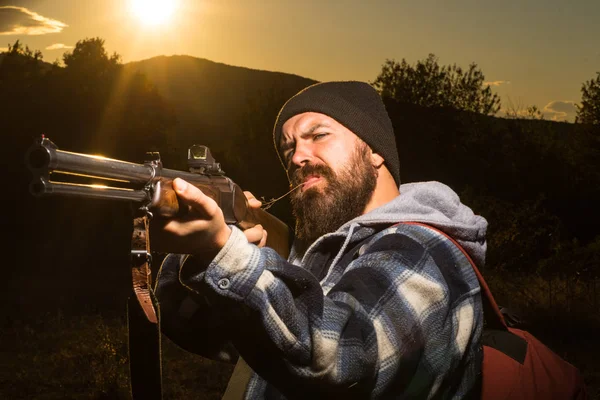 ひげを生やしたハンター男銃を押しながら森を歩きます。ライフル ハンターは、美しい夕日のシルエット。Autunm 狩り。山の狩猟。銃のバレル. — ストック写真