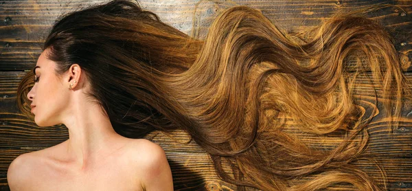 Cabello muy largo sobre fondo de madera. Hermosa modelo con peinado rizado. Concepto de peluquería. Productos para el cuidado y el cabello. — Foto de Stock