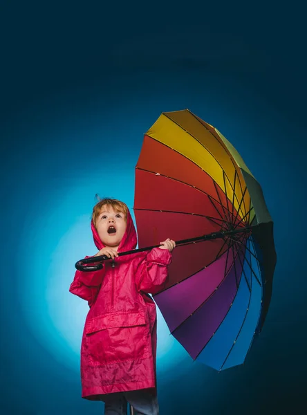 Niño bajo la lluvia. Lindo niño se están preparando para el otoño. Venta para toda la colección de otoño, increíbles descuentos. Niño alegre en impermeable con paraguas colorido . — Foto de Stock