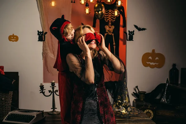 Mom and son play for all saints day in witchs costume at home. Family fun mother and child having fun and celebrate Halloween in devil costume. Beautiful young woman with child with pumpkins autumn. — Stock Photo, Image