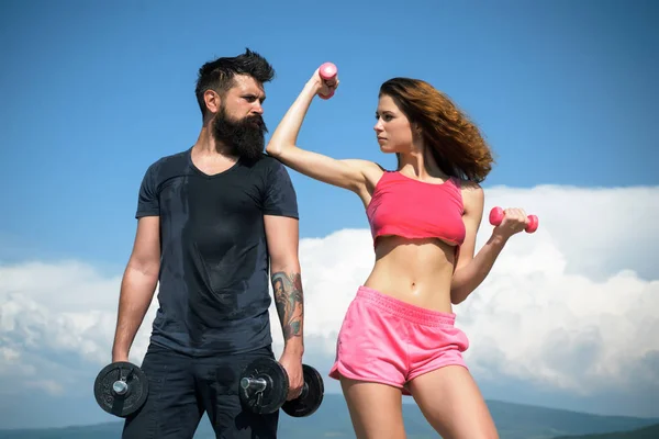 Pareja deportiva haciendo ejercicio con pesas sobre el fondo del cielo. Concepto de estilo de vida saludable. Hermosos amigos atractivos de fitness. Abdominales cuerpo de mujer fitness. Modelo femenino en ropa deportiva ejercitando al aire libre . —  Fotos de Stock