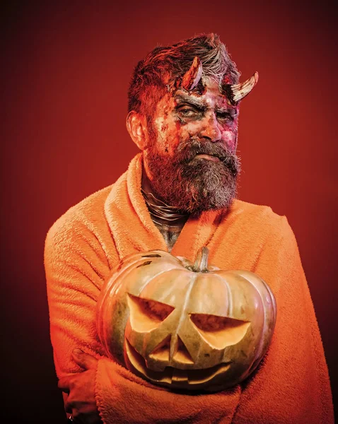 Хэллоуин человек дьявол держать тыкву на красном фоне — стоковое фото
