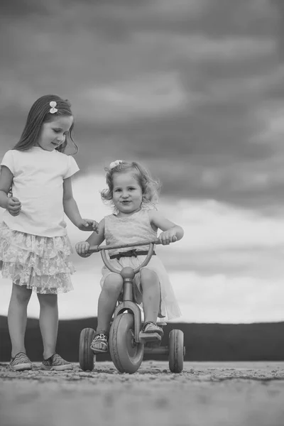 Ragazza giro triciclo con sorella su cielo nuvoloso — Foto Stock