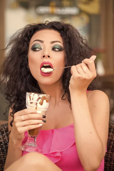 性漂亮的黑发女士与卷曲的头发和明亮的妆的肖像吃冷甜点的冰淇淋和咖啡卢达本纳从玻璃勺 垂直图片 — 图库照片