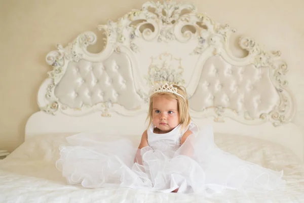 Princesa verdadeira. Acessório de cabelo. Menina usar coroa e penteado. Criança pequena com longos cabelos loiros. Pequena criança loira senta-se na cama. Penteados bonitos para meninas. Sua beleza brilha através — Fotografia de Stock