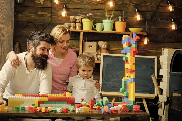 Pared de construcción de niño concentrado de bloques de plástico de colores. Sonriendo mamá y papá mirando a un niño adorable jugando con ladrillos de construcción. Hermosa mujer sosteniendo a su hijo y esposo por los hombros — Foto de Stock