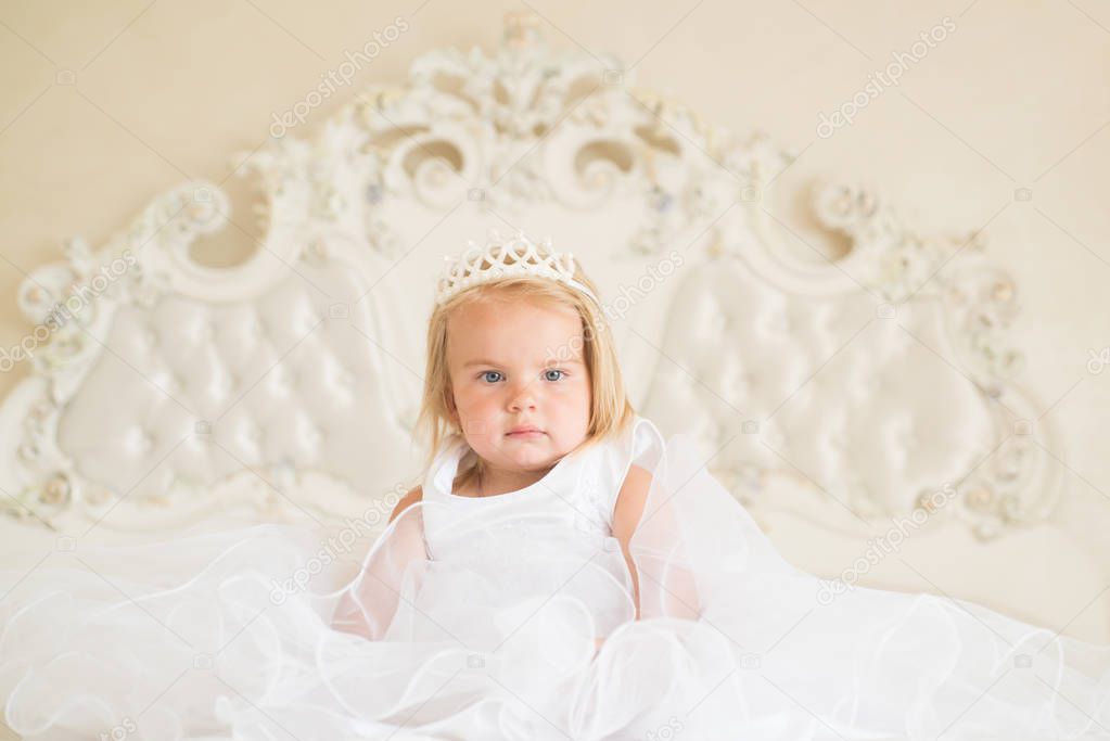 Fairytale princess. Small blond child sit on bed. Little girl wear tiara crown and hairstyle. Hair accessory. Little child with long blond hair. Beautiful hairstyles for baby girls. Be great every day