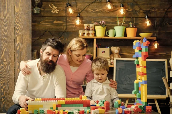 Los padres abrazos, ver jugar al hijo, disfrutar de la paternidad. Concepto de ocio familiar. Padre, madre e hijo lindo juegan con ladrillos constructores. Niño con los padres juegan con bloques de plástico, construir la construcción . —  Fotos de Stock