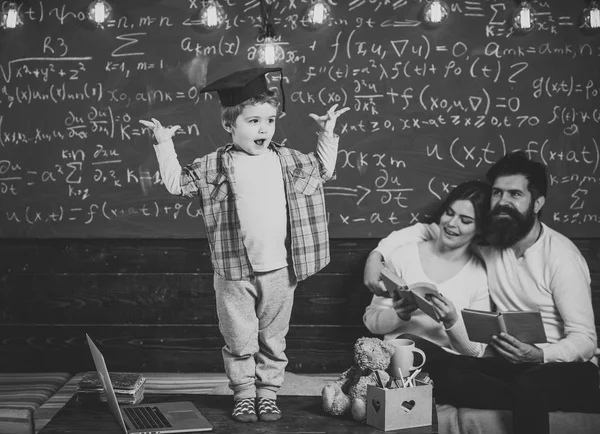 Έξυπνο παιδί απόφοιτος ΚΓΠ, όπως να εκτελέσετε. Αγόρι παρουσιάζοντας τις γνώσεις του με τη μαμά και τον μπαμπά. Οι γονείς που ακούει ο γιος τους, ελέγχοντας τα λάθη με το βιβλίο chalkboard σε φόντο. Προετοιμασία για εξετάσεις έννοια. — Φωτογραφία Αρχείου