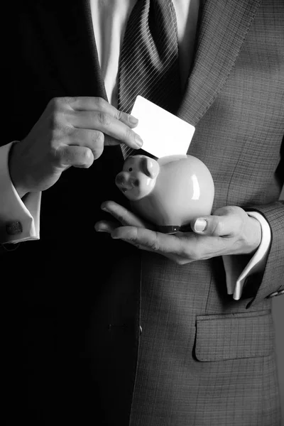 Male hands putting business card in piggy bank