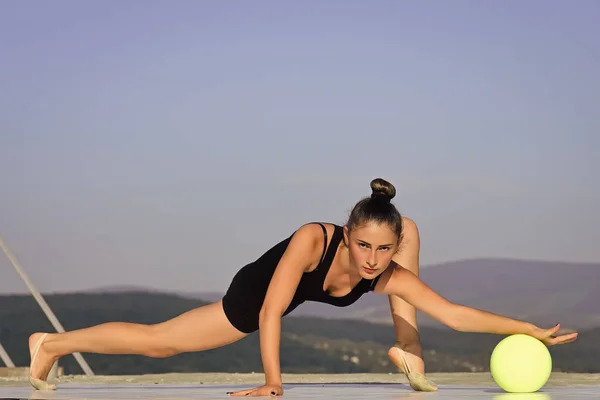 Vrouw gymnast in zwarte sportkleding met groene bal in split — Stockfoto