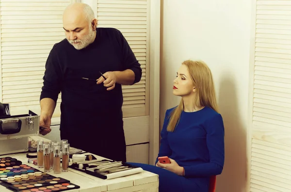 Hombre revisando el teléfono móvil con pinceles de maquillaje — Foto de Stock