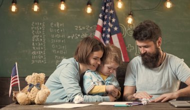 Anne oğlu Amerikan gelenekleri oynarken öğretim. Ebeveynler sınıf ABD bayrağı ile kara tahta arka plan ile evlat. Amerikan ailesinin oğlu ve ABD bayrağı ile masa başında oturmak. Vatansever eğitim kavramı.