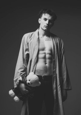 Romantik hediye ile bornoz adam. Adam sakin yüz, kas şekil, peluş yumuşak oyuncak ayı elinde tutar. Romantik maço kavramı. Çekici, koyu arka plan kas gövde, altı paketleri, adamla görünüyor.