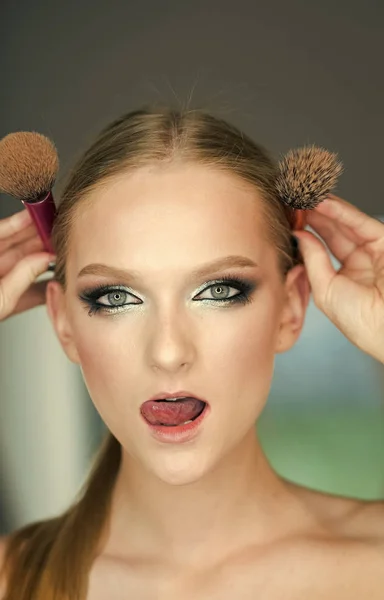 Dívka s mladou pleť obličeje, péče o pleť, mládež. Žena s tváří make-up drží štětce na hlavu. Žena s blond vlasy a make-up štětce, krása. Beauty model s glamour vzhled, účes — Stock fotografie