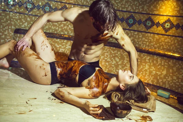 Muskularny mężczyzna sprawia, że masaż czekoladowy dla sexy kobieta w salonie — Zdjęcie stockowe