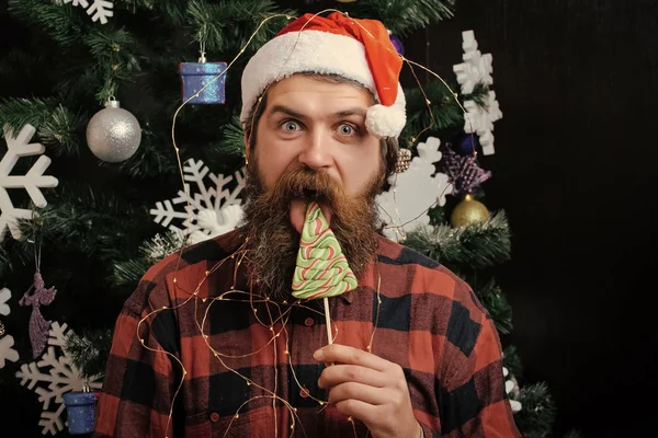 Karácsonyi férfi szakállal, boldog arc nyalja édességet nyalóka — Stock Fotó