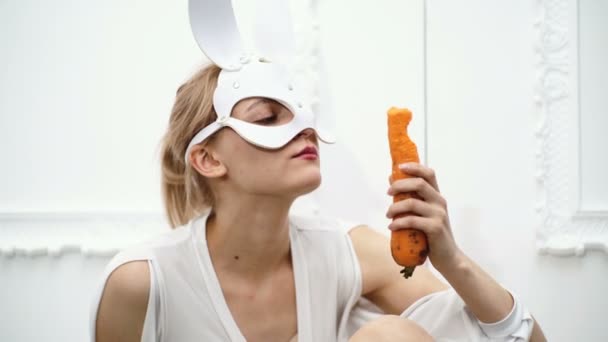Close up of a girl dressed in a mask of a hare that eats carrots on a white background. Concept of healthy food.