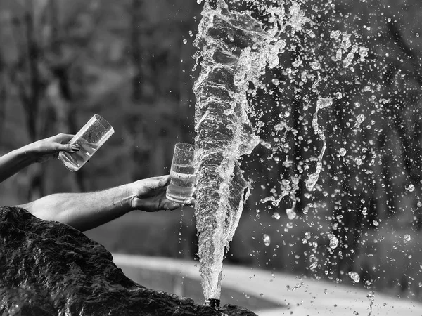 Mänskliga händer med glas nära fountain — Stockfoto