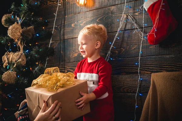 手にクリスマスプレゼントを持つサンタ帽子で笑う面白い子供。良いメリークリスマスとハッピーニューイヤー、挨拶と家庭の快適さから学びます. — ストック写真
