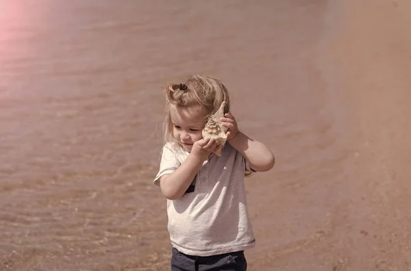 Dziecko słucha muszla w słoneczny dzień — Zdjęcie stockowe
