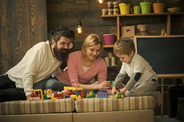 孩子与父母玩塑料积木, 建造建筑。关爱父母的理念。家庭在繁忙的面孔一起花费时间在娱乐室。父亲, 母亲和可爱的儿子玩构造砖. — 图库照片