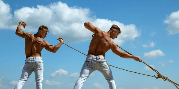 Fighting as a team. Twins men use muscular hand strength. Athletic twins with fit sexy body. Sport exercises for building strength and power. Strong men pull ropes