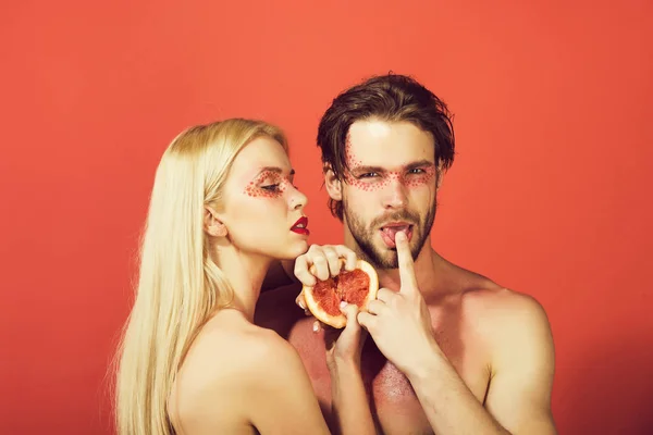 woman and man with creative fashionable makeup on face hold grapefruit fruit on red background, beauty and fashion, allergy, healthcare and vitamin, vegetarian and dieting, couple in love