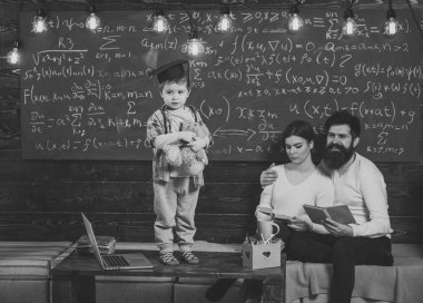 Çocuk Anne ve baba için onun bilgi sunma. Lisansüstü şapkalı akıllı çocuk gibi gerçekleştirmek. Oğulları, kara tahta arka plan dinleme anne. Destek kavramı. Çocuk oyuncak ayı ve gerçekleştirme tutar