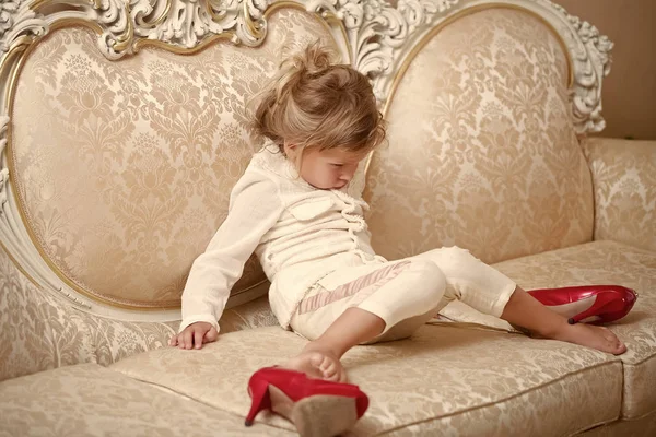 Малюк з нещасливим обличчям сидить на дивані з червоним взуттям — стокове фото