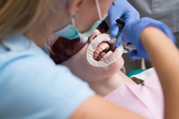 Close-up portrait of a female patient visiting dentist for teeth whitening in clinic. Dentist examining patients teeth in clinic. Teeth whitening.