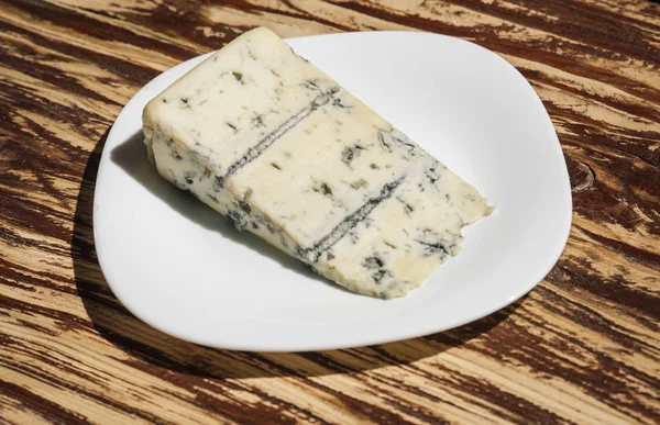 Мягкий и сливочный. Синий сыр. Кусок сыра на тарелке. Рокфор. Горгонзола. Итальянская или датская кухня на деревянном столе. Молочные продукты — стоковое фото