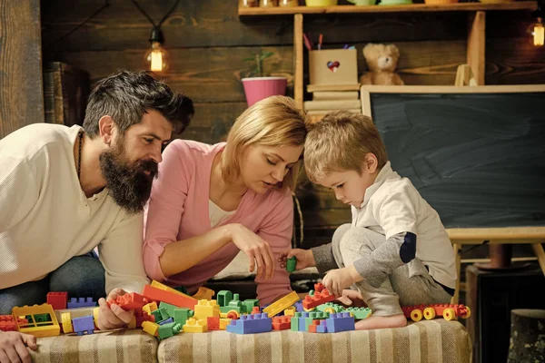 Padre, madre e hijo lindo juegan con ladrillos constructores. Niño con los padres juegan con bloques de plástico, construir la construcción. Familia en la cara ocupada pasar tiempo juntos en la sala de juegos. Concepto de padres cuidadores — Foto de Stock