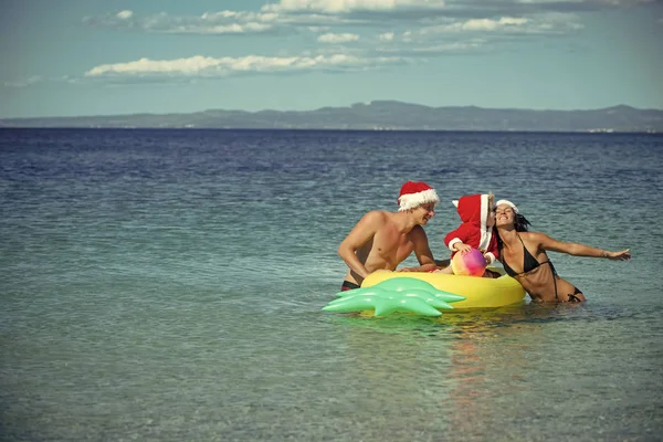 Weihnachtsfamilie mit Weihnachtsmütze am Strand mit Matratze — Stockfoto