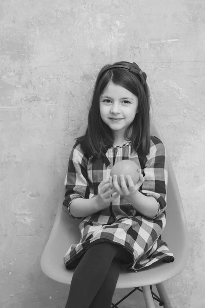 Menina com laranja na mão sentado na cadeira de plástico — Fotografia de Stock