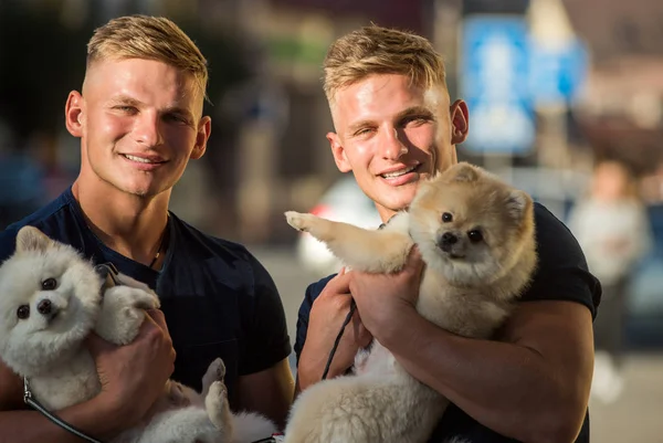 Happy family on walk. Spitz dogs love the company of their family. Twins men hold pedigree dogs. Muscular men with dog pets. Happy twins with muscular look