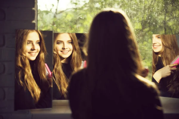 Meisje met lang haar blik op spiegel met kam — Stockfoto