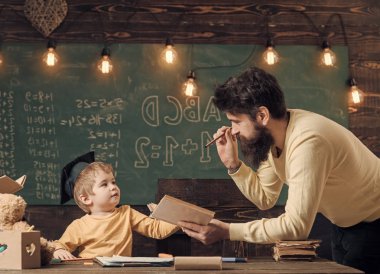 Harika çocuk ve dahi kavramı. Baba, öğretmen okuma kitabı, öğretim çocuk, evlat, kara tahta arka plan. Baba dahi oğlumu büyümek istiyor. Lisansüstü şapkalı çocuk çocuk dinleme babama seviyor.
