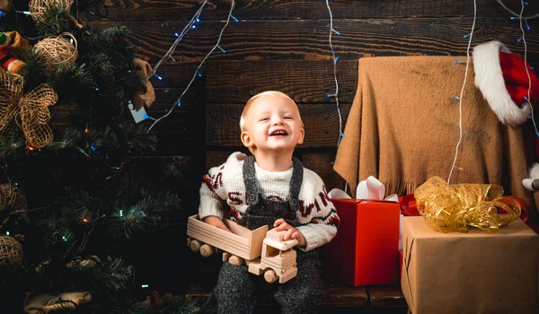 Słodkie małe dziecko otwierając obecne w pobliżu choinki. Wesołych Świąt i szczęśliwego nowego roku. Chłopiec dziecko się śmiać i cieszyć się darem. Świąteczne marzenie — Zdjęcie stockowe