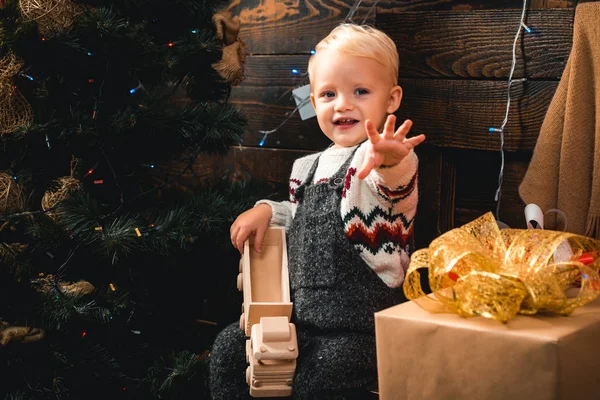 С Рождеством и Новым годом. Милый маленький ребенок, открывающий подарок возле рождественской елки. Мальчик смеется и наслаждается подарком . — стоковое фото