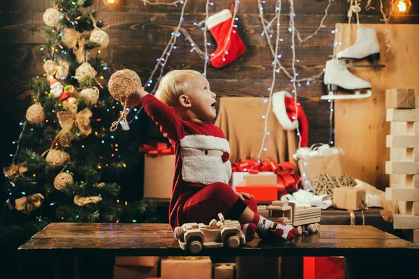 クリスマスの幼年期。メリー クリスマスと新年あけましておめでとうございます。クリスマス ツリーの背景色のかわいい小さな子供。笑いと贈り物を楽しんでの子の少年。クリスマスのおもちゃ. — ストック写真