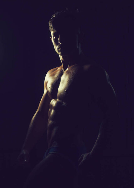 Muscular young man with athletic bare body standing on black background