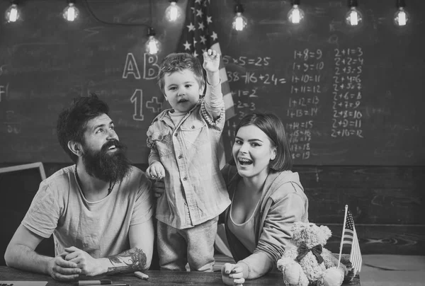 Kid with parents in classroom with usa flag, chalkboard on background. Patriotic education concept. American family sit at desk with son and usa flag. Parents teaching son american traditions playing. — Stock Photo, Image