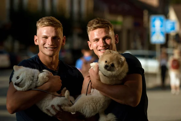 Dogs bring them joy. Muscular men with dog pets. Happy twins with muscular look. Twins men hold pedigree dogs. Spitz dogs love the company of their family. Happy family on walk