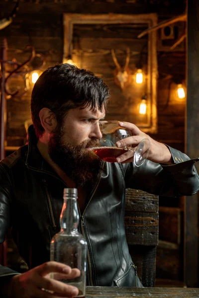 Alcohol addiction. Bearded man drinking whiskey, brandy or cognac. Pub retro vintage interior. Hipster barman concept. Swag guy with alcohol. Drunk man.