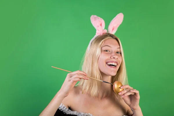 魅力的な若い女性の身に着けているバニーの耳と緑色の背景に分離されたイースターエッグを抱えています。幸せな人。イースターのウサギ。美しい官能的な女性のファッションの肖像画. — ストック写真